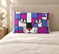 A rectangular throw pillow featuring a colorful, geometric cat face design in shades of purple, blue, white, black, and orange, resting on a beige bed with a matching headboard.