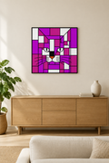 A framed square wall art print featuring a stylized cat face in geometric purple, magenta, white, black, and orange blocks, displayed above a light wood sideboard in a modern living room setting.